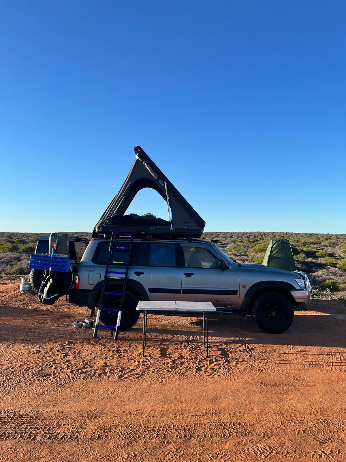 Side view of the Nissan Patrol camper parked on a red dirt track.