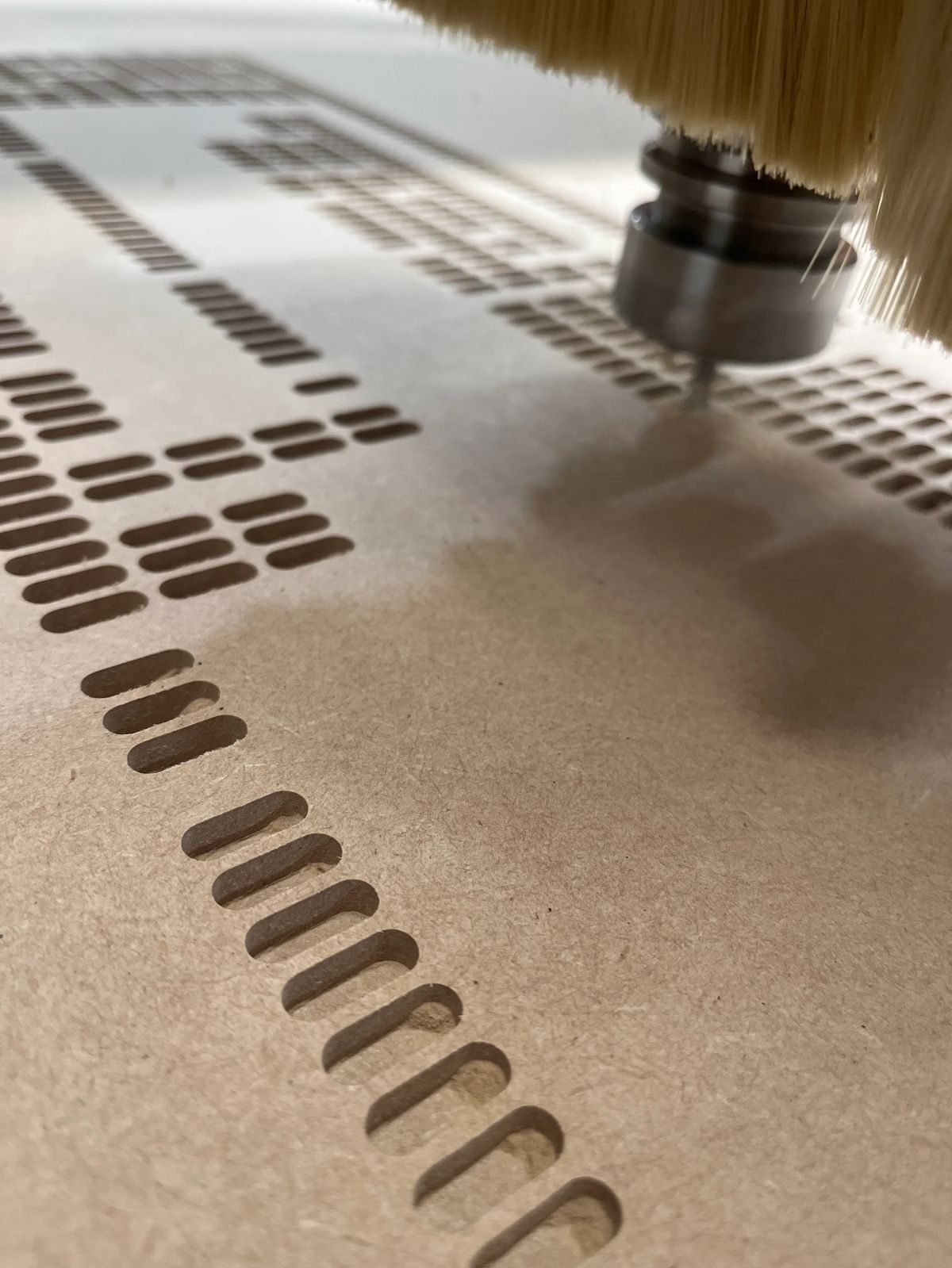 Close view of a CNC router cutting a repeating pattern into a wooden panel.