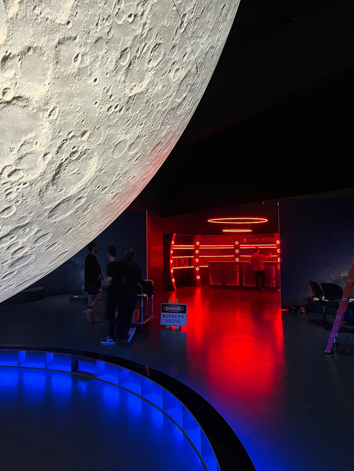 To The Moon interior with a moon backdrop, blue lighting and a red-lit installation.