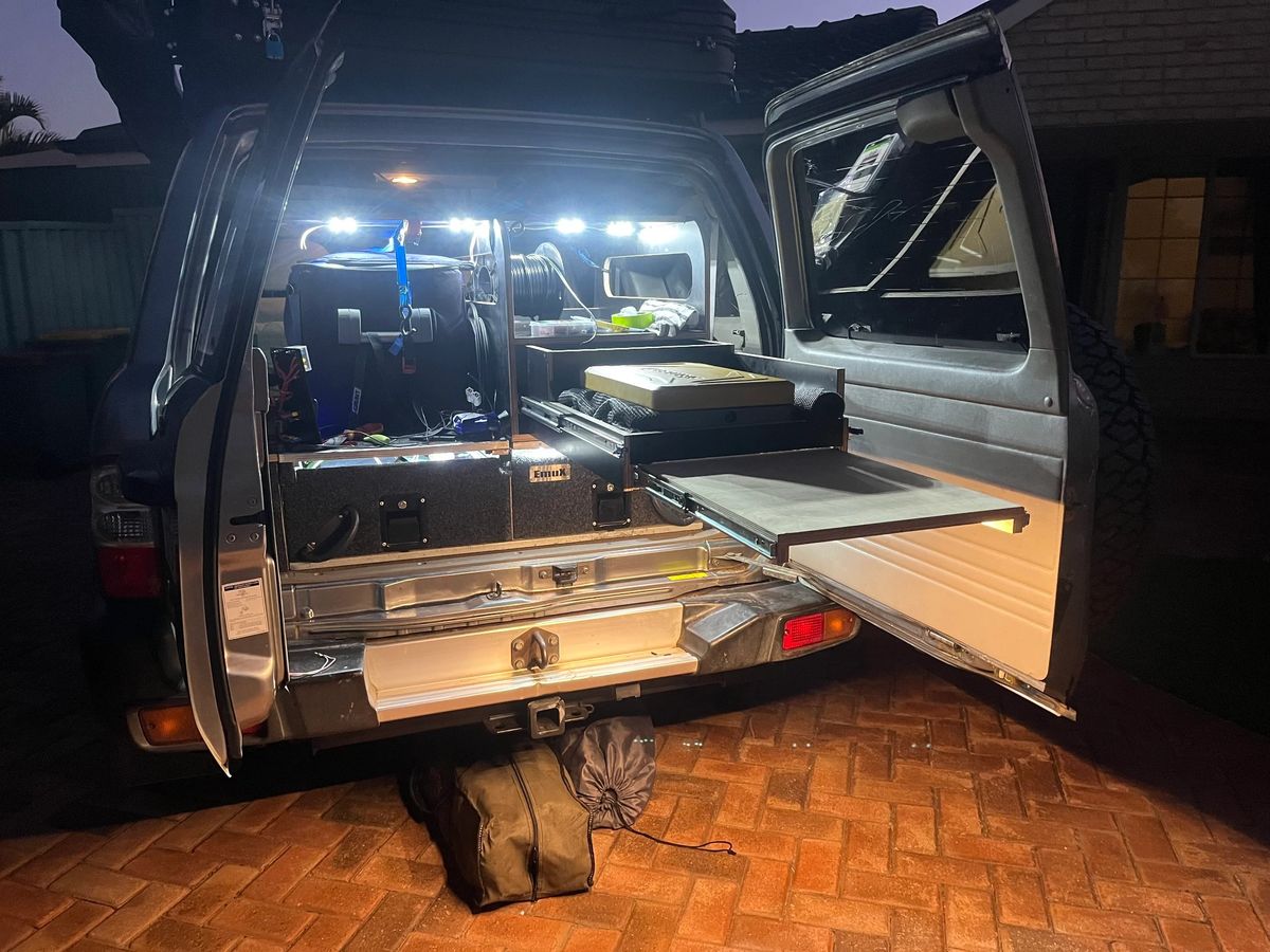 Nissan Patrol rear hatch open at night, showing the camper kitchen and interior lights.